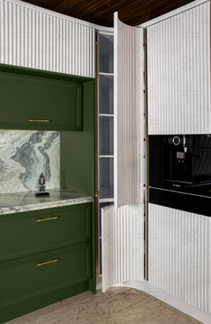 نمای نزدیک از کابینت کنج با درب منحنی باز شده، طراحی سفید شیار‌دار و فضای داخلی قفسه‌بندی‌شده