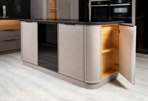 جزیره‌ی آشپزخانه با کابینت منحنی و درب باز، نمایانگر فضای داخلی و طبقه‌بندی چوبی