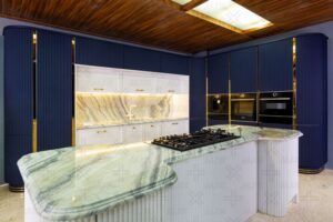 فضای داخلی آشپزخانه با سقف چوبی، نور سقفی و ترکیب رنگ سفید و سرمه‌ای