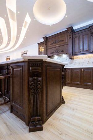 نمای داخلی آشپزخانه با صفحه رویه روشن و کابینت چوبی حکاکی‌شده