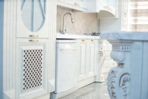 کابینت کلاسیک رنگ روشن با طراحی شبکه‌ای و سینک استیل در کنار آن