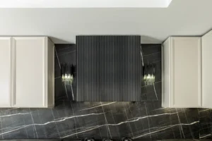 هود آشپزخانه در طراحی نئوکلاسیک، با ظاهری مدرن و خطوط مینیمالیستی، که بر روی پس‌زمینه‌ای از کاشی‌های مشکی و طرح‌های سفید قرار دارد. این هود با طراحی ساده و شیک خود به‌خوبی با فضای آشپزخانه‌های نئوکلاسیک هماهنگ می‌شود و جلوه‌ای مدرن و در عین حال کلاسیک به محیط می‌بخشد