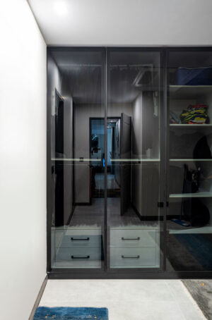طراحی لاکچری اتاق کمد با ترکیب کشوهای خاکستری، ریل‌های لباس، قفسه کیف و بخش ویژه نگهداری نوشیدنی.