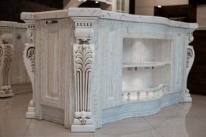 کابینت سفید ساده با روکش چوب و جزیره بزرگ سنگی، طراحی مینیمال با دستگیره‌های طلایی.