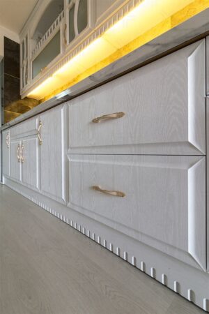 کابینت آشپزخانه سفید با روکش چوب و دستگیره‌های طلایی، همراه با نورپردازی زیر کابینتی
